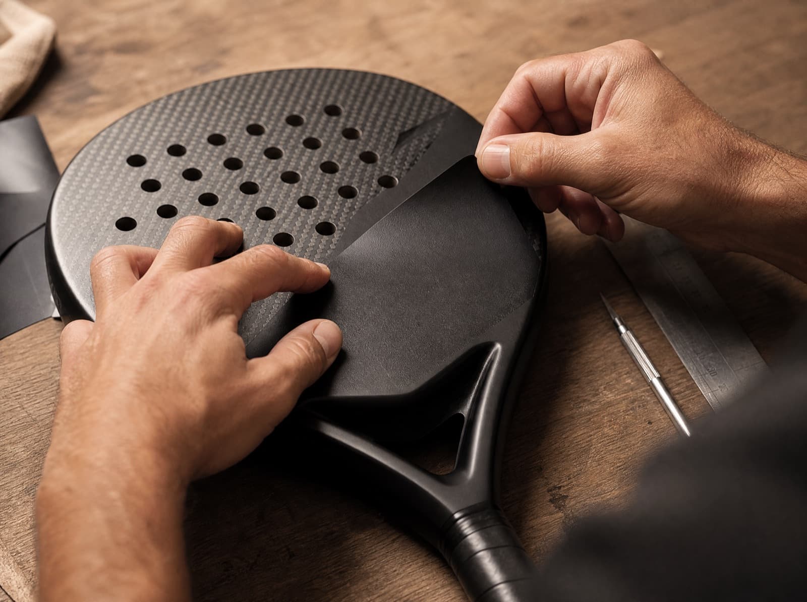 Hände in der Werkstatt bringen eine matte schwarze Folie auf einen Custom Padelschläger auf
