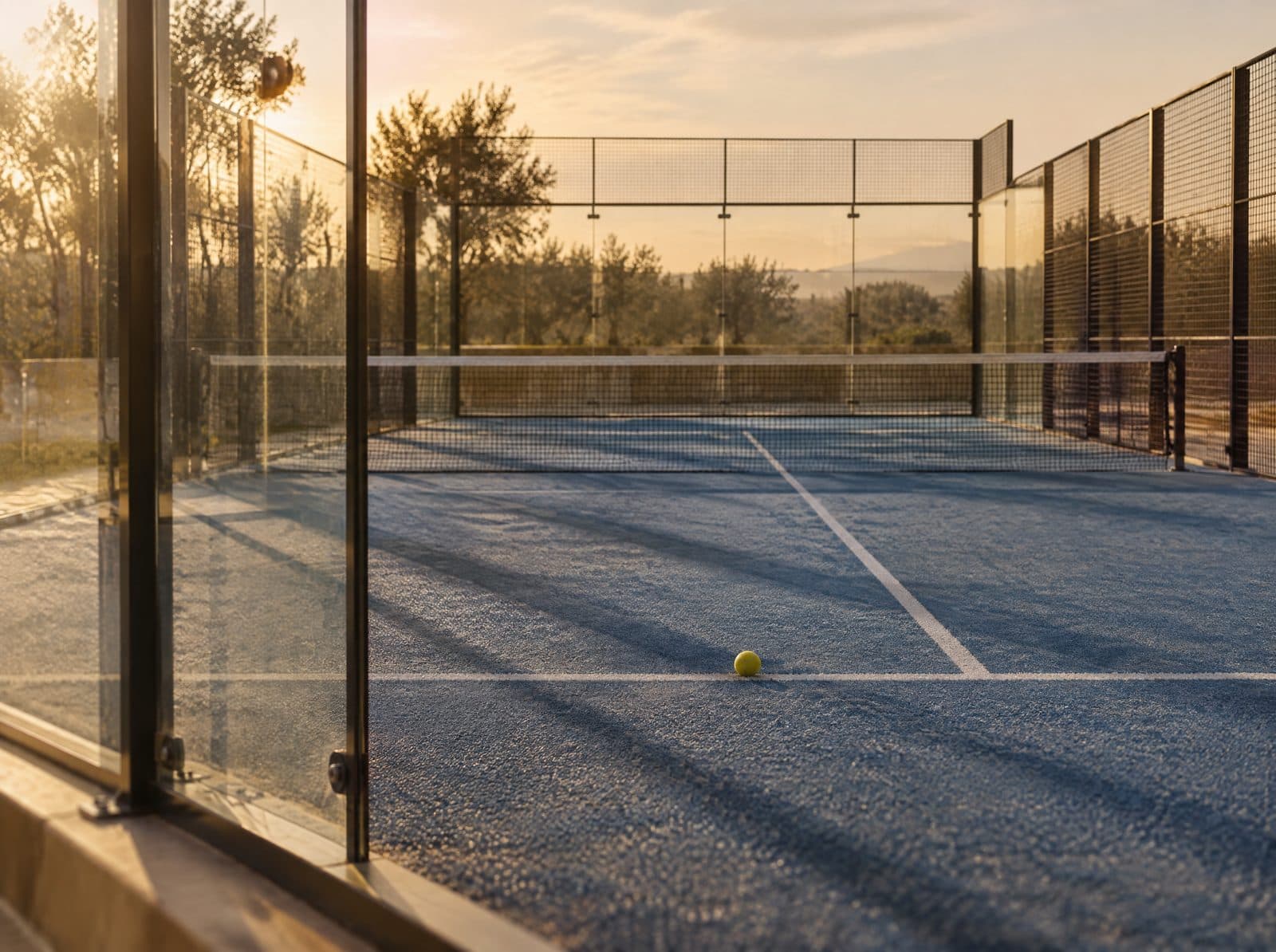 Terrain de padel vide avec des vitres et un filet dans une lumière de fin de journée