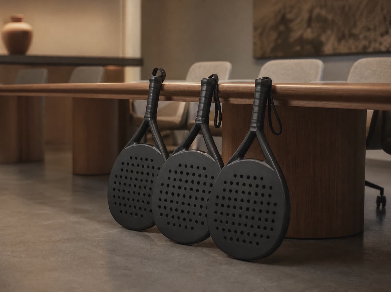 Three custom padel rackets side by side against a meeting room table