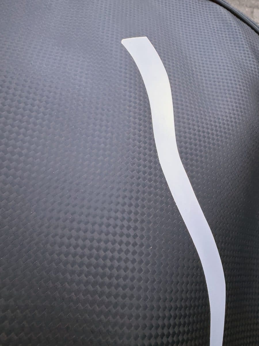 Close-up van een witte sticker op een zwarte hoes in carbonlook